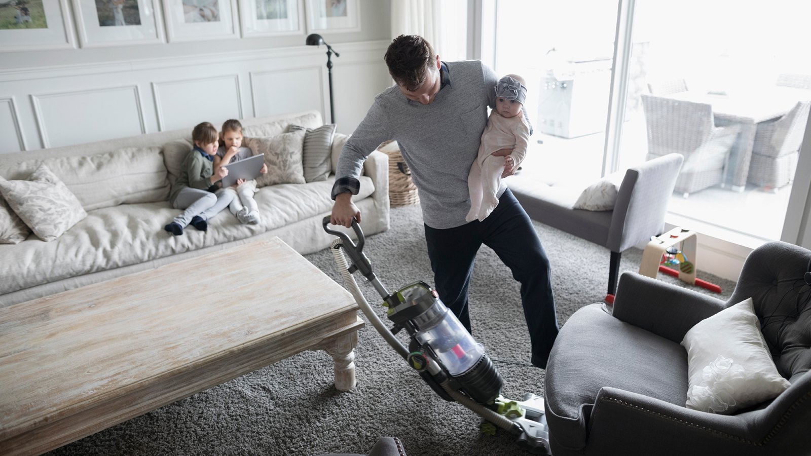 Father holding baby daughter and vacuuming living room