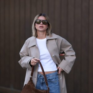 BERLIN, GERMANY - APRIL 01: Sophia Geiss seen wearing Vehla Eyewear black / brown dark sunglasses, Drykorn white cotton basic casual cropped top, Meotine beige oversized trench coat adds effortless elegance, COS blue denim oversized, loose-fitting, wide-leg jeans with a drawstring waist enhance the relaxed vibe and a brown suede leather vintage bag complements the western aesthetic, on April 01, 2025 in Berlin, Germany. (Photo by Jeremy Moeller/Getty Images)