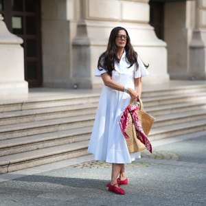 FRANKFURT AM MAIN, GERMANY - JULY 10: Angelika Hanel is seen wearing a white short-sleeved shirt midi dress with a flared silhouette and soft pleating from Erika Cavallini; a pair of signature Alaïa ballet flats in red fishnet textile and patent leather, a buckle strap on top and round toes from Alaïa; the ICARE maxi shopper crafted from hand-embroidered natural raffia and a brown gold oversized, sculptured Cassandre from Saint Laurent adorned with a red and white silk bandana from Arket tied to the handle; a silver Rolex Daytona watch; a yellow golden Juste un Clou bracelet from Cartier; a pavé diamond Tennis bracelet; a bold sterling silver Bone Cuff from Tiffany & Co.; oversized black aviator sunglasses with orange shaded glasses from Kapten & Son; long brown hair and natural make-up on July 10, 2025 in Frankfurt am Main, Germany. (Photo by Moritz Scholz/Getty Images)