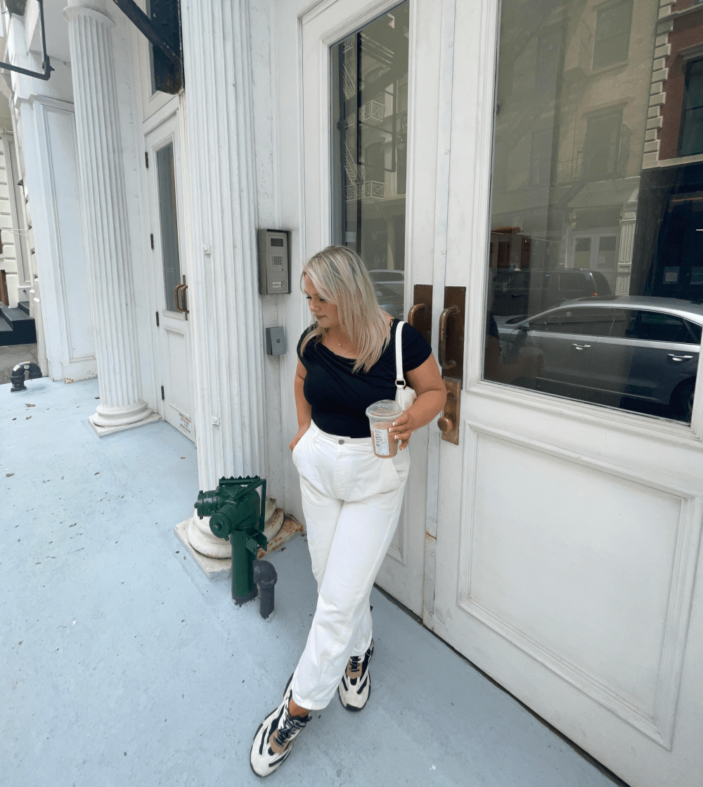 woman wearing black top, white pants, and tennis shoes on NYC street
