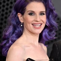 Kelly Osbourne with Curly Purple Hair Smiling and Looking at Camera in Black Top Sheer Dress