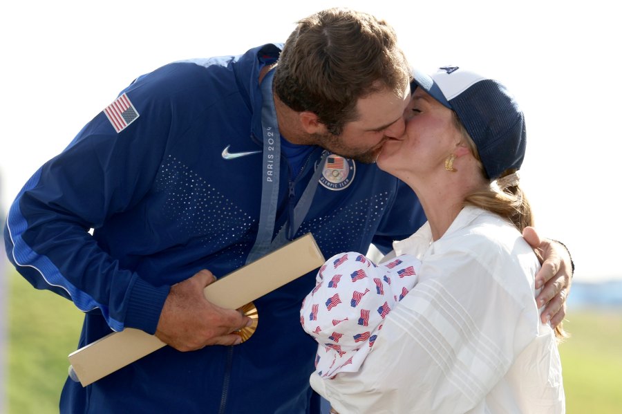 Scottie Scheffler of Team USA kisses wife Meredith Scheffler as she carries their son, Bennett Scheffler following his Olympic win.