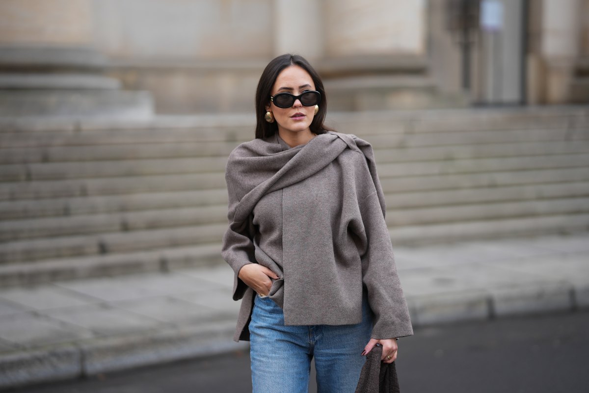 Laura Noltemeyer is seen wearing a taupe fine-knit sweater with a sculptural draped front collar from Zara; light-blue straight-leg denim jeans with a soft fading from Zara; beige suede winter boots with a rounded toe, rope laces, tonal stitching and a thick rubber sole from Inuikii;a large textured dark-brown shoulder bag in a soft sculptural, slouchy shape and woven leather from Les Visionnaires x Michi from the Want; black oval sunglasses with a glossy acetate frame and dark lenses from Celine; chunky gold sculptural earrings from Zara; dark brown soft leather gloves from Zara; her dark brown hair is worn straight with a middle parting, tucked behind the ears on November 25, 2025 in Berlin, Germany.