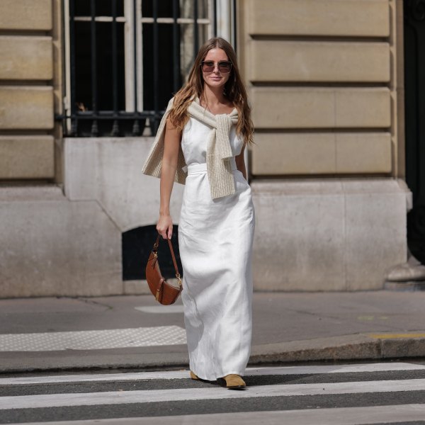Diane Batoukina wears dark brown large squared sunglasses from Dior, a white square-neck / linen belted long dress, a white latte ribbed wool pullover knot at the shoulder, a camel brown shiny leather crocodile print pattern handbag from Ralph Lauren, brown suede block heels / pointed ankle boots , during a street style fashion photo session, on April 28, 2023 in Paris, France.