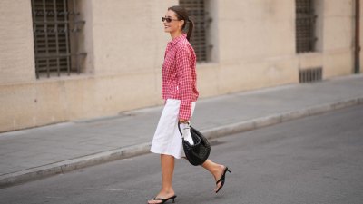 MUNICH, GERMANY - JUNE 8: Lina Uhrig is seen wearing a pink and red cotton checked cropped shirt with a button front closure, long sleeves, pointed collar, loose fit silhouette and small check pattern from JJXX; white cotton Bermuda shorts with a straight silhouette, knee length, clean waistband and minimal design from Stradivarius; black leather kitten heel sandals with thin toe straps, open toe construction and low slim heels from Stradivarius; a natural pedicure visible through the sandals; a black woven leather shoulder bag with a compact curved silhouette, short top handles, textured woven surface and metal hardware details from Adax; gold tone hoop earrings; rectangular black acetate sunglasses with narrow frames and dark tinted lenses from Chimi; her brown hair is worn in a sleek low ponytail with a center part; with natural make up on June 8, 2026 in Munich, Germany. (Photo by Moritz Scholz/Getty Images)