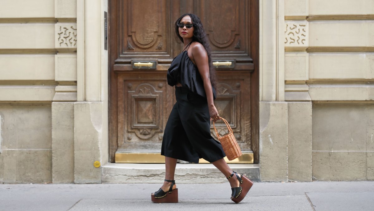 PARIS, FRANCE - JULY 19: Carrole Sagba wears long wavy black hair, black oval sunglasses, a black gathered cropped halterneck top by NA-KD, black culottes long shorts by Uniqlo, a natural wicker bucket bag by Parfois, black leather platform wedge sandals with wooden soles and gold-tone stud embellishments by Zara, gold-tone rings, during a street style fashion photo session, on July 19, 2026 in Paris, France. (Photo by Edward Berthelot/Getty Images)