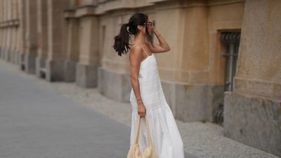 Aylin Sengül is seen wearing a white spaghetti-strap maxi dress with textured horizontal panels and a gathered hem by COS; brown leather “Oran” sandals by Hermès; a raffia shoulder bag with a slouchy hobo shape by COS; a delicate gold-tone necklace; a rose gold “Knot” bracelet by Celine; a vintage tennis bracelet; a slim silver-tone bangle; a gold ring; slim oval dark tortoiseshell sunglasses by Chanel during Berlin Fashion Week Spring/Summer 2027 on July 4, 2026 in Berlin, Germany.