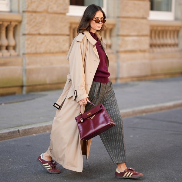 DUESSELDORF, GERMANY - AUGUST 19: Patricia Wirschke is seen wearing a Anna V Berg burgundy knit polo sweater with three buttons, collar and ribbed hem; a classic beige long Herno trench coat, with a notched collar, storm flap, and belted cuffs; a pair of high-waisted, wide-leg, ankle length Rossi pants that feature a gray pinstripe pattern with tailored pleats and loose silhouette; a pair of burgundy suede Adidas Samba X Wales Bonner sneakers with cream stripes; a structured, glossy burgundy leather Hermes Kelly bag with gold-tone hardware; a pair of Miu Miiu oval-shaped tortoiseshell sunglasses; her brown hair is styled in a straight, shoulder-length look with a middle part on August 19, 2025 in Duesseldorf, Germany. (Photo by Moritz Scholz/Getty Images)